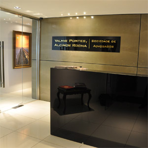 O balcão espelhado e o porcelanato refletem a iluminação e os móveis que compõem a recepção do escritório em Fortaleza/CE. 
